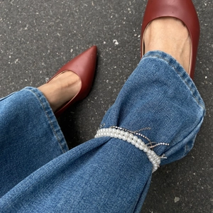 Mehrlagiger Fußschmuck mit Kunstperlen und Kreuzanhänger an Jeans-Saum-Detail