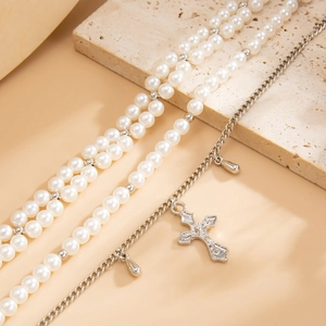 Nahaufnahme der Lagen-Fußkette mit Kunstperlen, silbernem Kreuz und Metallanhängern