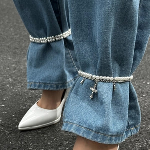 Fußkette mit Kunstperlen und Kreuzanhänger als stylisches Accessoire an einer Jeanshose