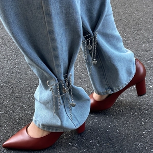 Detail of silver heart charm pin with metal chains attached to denim jeans cuff