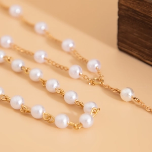 Macro di una collana a catena dorata con perle rotonde su sfondo caldo minimalista