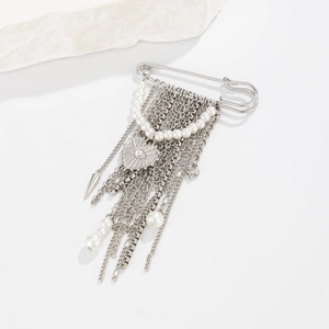 Dettaglio di una spilla in argento con catene multistrato, perle e ciondolo a forma di cuore