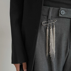 Dettaglio di spilla con nappe in metallo argento usata come accessorio decorativo per pantaloni