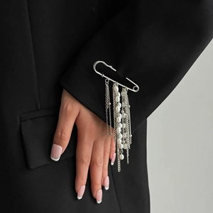 Dettaglio di una spilla in argento con lunghe catene di metallo e perle bianche