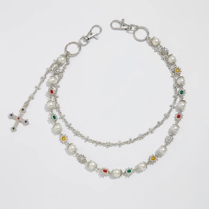 Macro detail of silver pants chain with faux pearls, colorful crystal flowers and cross