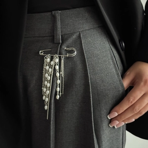 Dettaglio spilla da balia in metallo argento con lunghe nappe di perle su pantaloni grigi