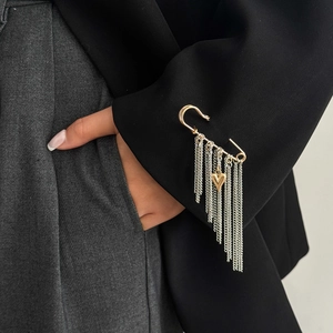 Dettaglio della spilla a balia con nappe a catena argentata sulla manica nera di un blazer