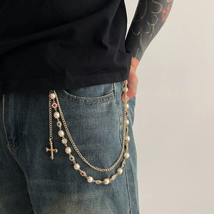 Detail of gold chain belt with faux pearls and a colorful rhinestone cross pendant on jeans