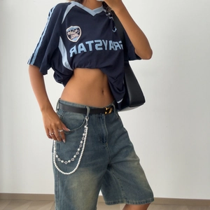 Detail of layered waist chain with faux pearls and cross charms on denim shorts