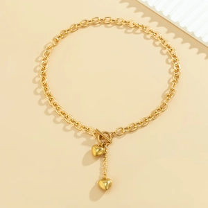 Detail van een gouden ketting met dubbele hartvormige hangers en OT-kapittelsluiting