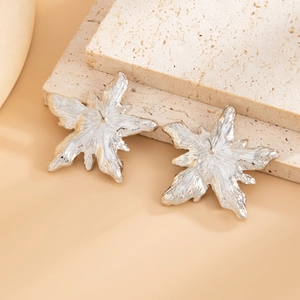 Macro detail of silver liquid lava textured star earrings on a warm beige stone