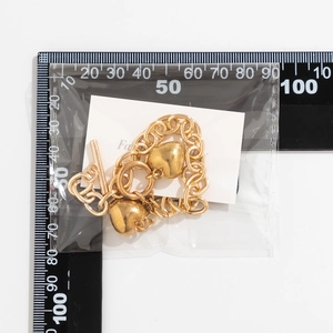 Detail van gouden schakelarmband met hartjes en een OT-sluiting op een witte kaart