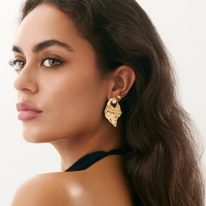 Macro detail of liquid lava textured gold metal earring with a white pearl on a model