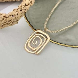 Nahaufnahme des goldenen geometrischen Spiralanhängers an einer champagnerfarbenen Kette