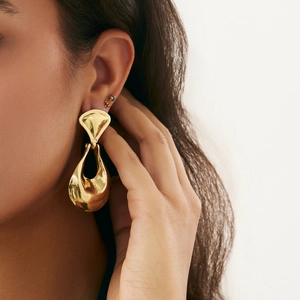 Close-up of a large gold liquid-metal style drop earring with a high-polished mirror finish
