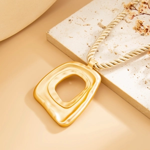Makroaufnahme eines mattgoldenen hohlen geometrischen Anhängers an einer Seilkette