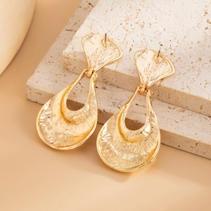 Macro shot of gold liquid lava textured drop earrings on a minimalist stone display