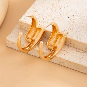 Close-up of golden sculptural molten metal earrings displayed on white travertine stone