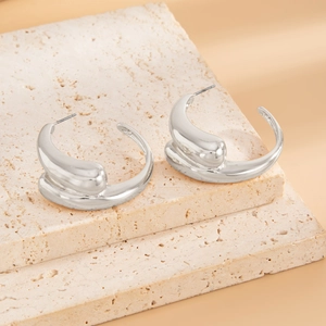 Close-up of silver-tone liquid lava metal C-shaped earrings on textured stone
