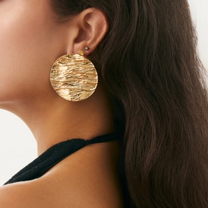 Detailed close-up of large golden disc earrings with irregular pleated metal texture