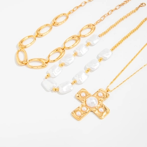 Detail goldener Halsketten mit Perlenkreuz-Anhänger und Gliederketten auf weißem Grund