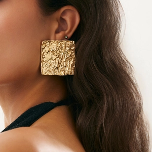Detailed view of large gold square earrings with hammered lava texture on model