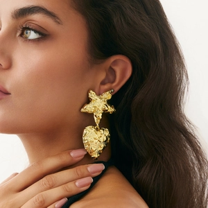 Macro shot of large liquid lava gold heart and star earrings on model showing metal texture