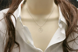 Detail van een zilveren golfketting met cirkelvormige hanger op een wit overhemd