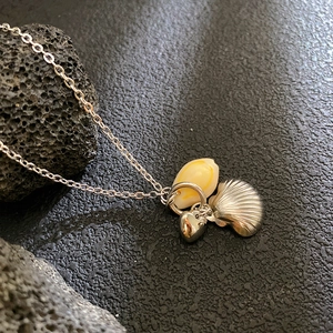 Collana con cuore in conchiglia e ciondolo a ventaglio su fondo in roccia lavica