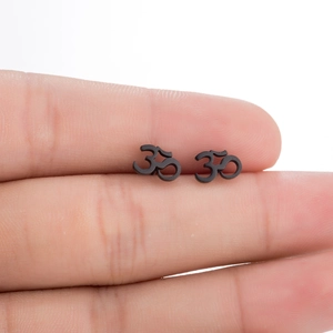 Détail macro de petites boucles d'oreilles Om noires tenues entre les doigts pour l'échelle