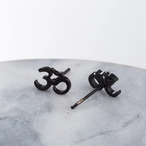 Détail macro de boucles d'oreilles Om noires sur marbre, montrant les bords métalliques