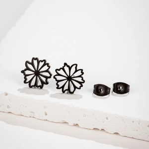 Détail de boucles d'oreilles fleurs noires ajourées sur un support en pierre blanche