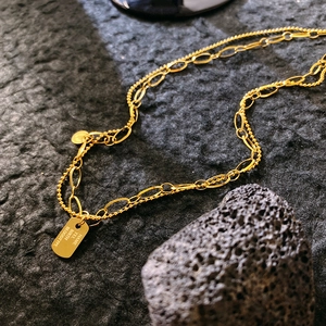 Double-layered gold pendant necklace with engraved rectangular tag on volcanic stone