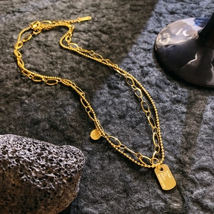 Double-layered golden necklace featuring coin and rectangle pendants on volcanic stone