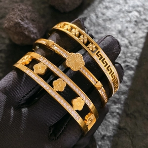 Three elegant gold-plated clover bangles with zircon stones on a dark stone background