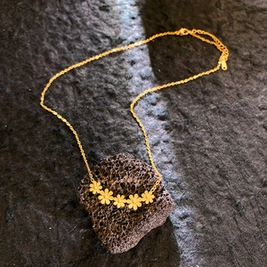 Collier marguerite doré avec cinq breloques fleurs sur fond de pierre noire texturée
