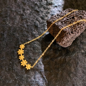 Élégant collier doré avec cinq pendentifs marguerites sur fond de pierre volcanique
