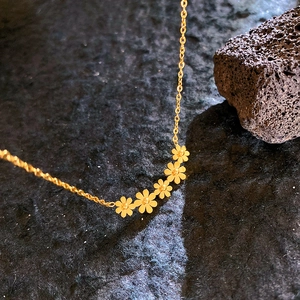 Collier doré élégant orné de cinq petites marguerites sur un fond sombre texturé