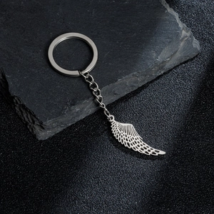 Minimalist stainless steel keychain with detailed hollow angel wing pendant on stone background
