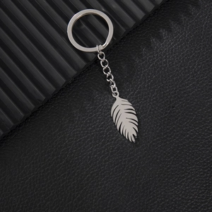 Minimalist stainless steel keychain with feather pendant on a black leather background