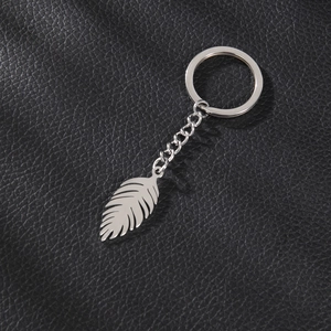Minimalist silver stainless steel feather pendant keychain on black leather surface