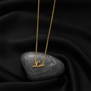 Détail macro du collier lettre Lion doré sur fond de soie noire et galets élégants