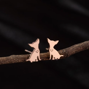 Detalle de pendientes de perro en oro rosa con recorte de corazón sobre una rama oscura