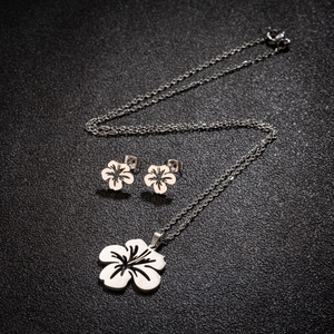 Ensemble collier et boucles d'oreilles fleur en acier inoxydable sur fond sombre texturé