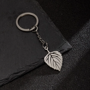 Minimalist silver stainless steel hollow leaf pendant keychain on a dark stone surface
