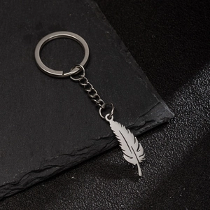 Polished stainless steel feather pendant keychain on elegant dark stone and leather surface