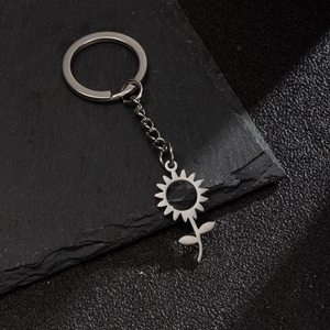Detailed view of sunflower metal keychain on black stone surface with textured background