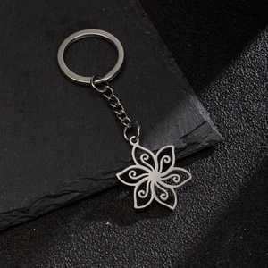 Silver stainless steel daisy flower keychain with hollow carved petals on stone surface