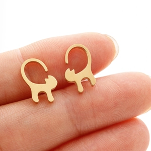 Macro shot of minimalist gold cat stud earrings on a fingertip for size reference