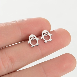 Macro detail of cute stainless steel penguin stud earrings held on a fingertip